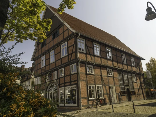 Haus Ottens Ein historisches Fachwerkhaus mit roten Ziegeln und weißen Fensterrahmen, umgeben von Herbstlaub.