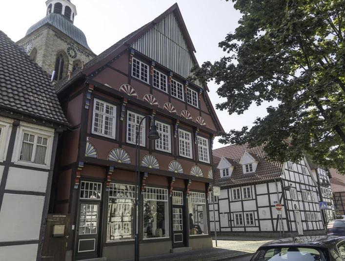 Fachwerkhaus mit roten Akzenten, großer Schaufensterfront, daneben weitere historische Fachwerkbauten.