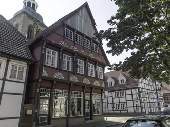 14-08 14-08 Rheda-Wiedenbrück-0385.jpg Fachwerkhaus mit roten Akzenten, großer Schaufensterfront, daneben weitere historische Fachwerkbauten.