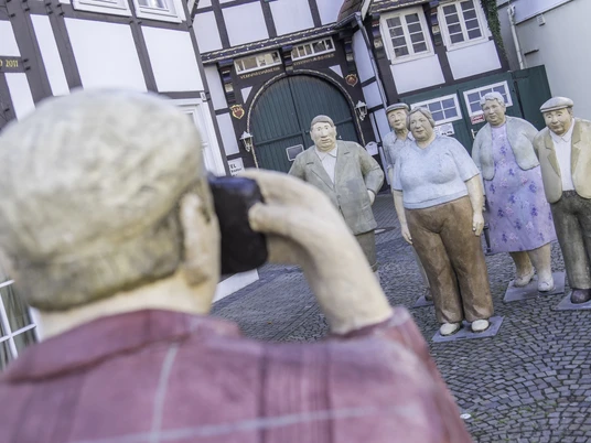 Eine lebensgroße Figurengruppe posiert für ein Foto, aufgenommen von einer Statue eines Fotografen.