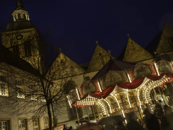 Historischer Weihnachtsmarkt bei Nacht mit Karussell und erleuchteten Gebäuden vor einem Kirchturm.
