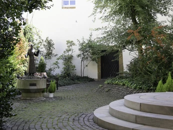 Kloster Wiedenbrück Innenhof mit Kopfsteinpflaster, flankiert von Pflanzen und einer Statue eines Franziskanermönchs.