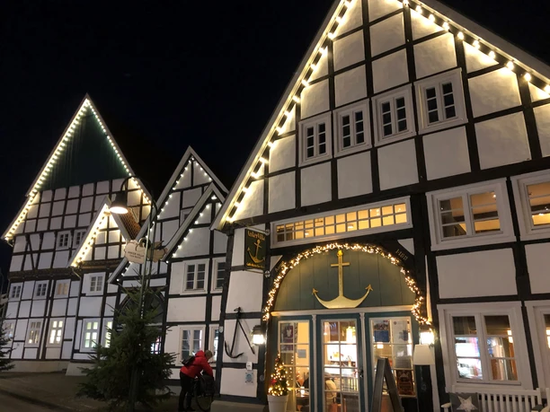 Fachwerkgebäude mit festlicher Beleuchtung in der Nacht, Menschen davor, winterliche Stimmung.