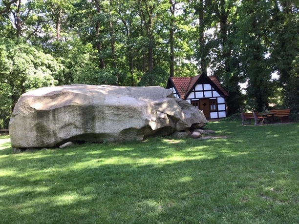 Großer Stein (neu).jpg Großer Stein bei Melle: Ein mächtiger Felsbrocken neben einer Fachwerkhütte im schattigen Wald.