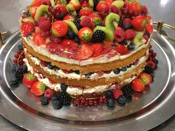 Eine mehrschichtige Torte mit frischen Beeren und Kiwischeiben auf einem silbernen Tablett.