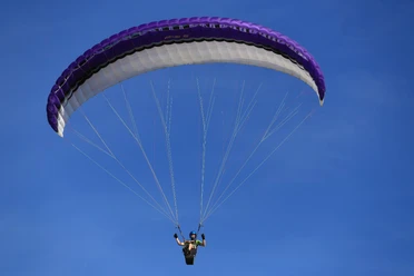 Gleitschirmflieger schwebt am klaren blauen Himmel, der violette Schirm öffnet sich majestätisch über ihm.