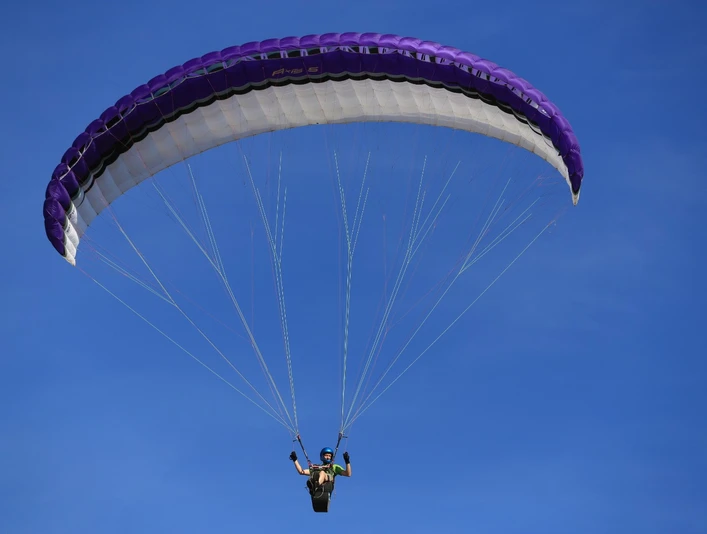 Gleitschirmflieger schwebt am klaren blauen Himmel, der violette Schirm öffnet sich majestätisch über ihm.