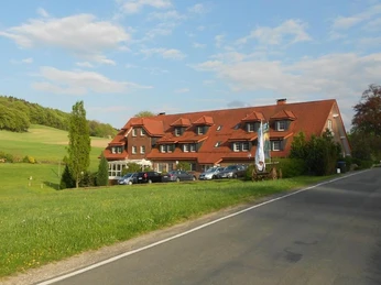 Halle_Hotel Rehkitz_Aussenansicht_A Kraft.jpg Mehrstöckiges Hotelgebäude mit roten Dächern und grüner Landschaft im Hintergrund.