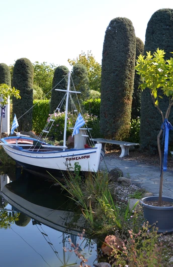 Ein traditionelles griechisches Boot liegt an einem ruhigen Teich, umgeben von mediterraner Vegetation.