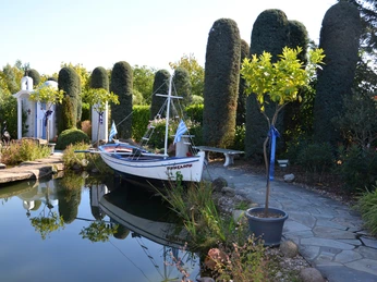 Ein traditionelles griechisches Boot liegt an einem ruhigen Teich, umgeben von mediterraner Vegetation.