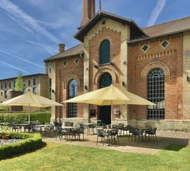 Abrahams_6.jpg Historische Backsteinarchitektur mit großer Terrasse, Sonnenschirmen und einladenden Sitzplätzen im Freien.