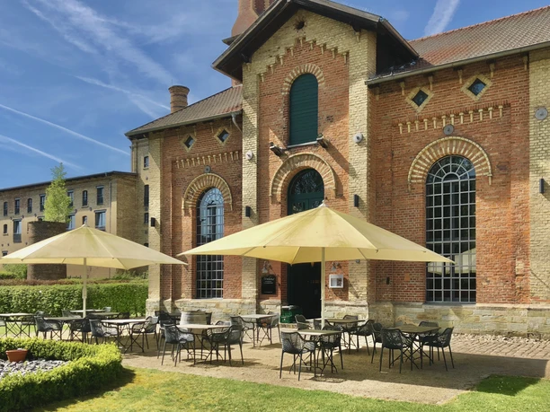Abrahams_6.jpg Historische Backsteinarchitektur mit großer Terrasse, Sonnenschirmen und einladenden Sitzplätzen im Freien.
