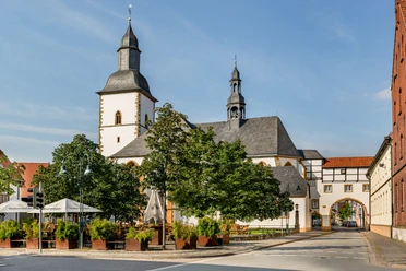 Historische Kirche mit zwei Türmen, umgeben von Bäumen in einer malerischen Stadtlandschaft.