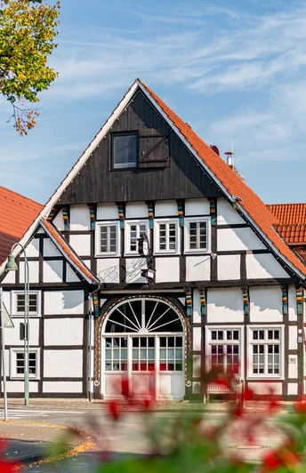 Fachwerkhaus mit roten Dächern und blühenden Pflanzen im Vordergrund an einem sonnigen Tag.