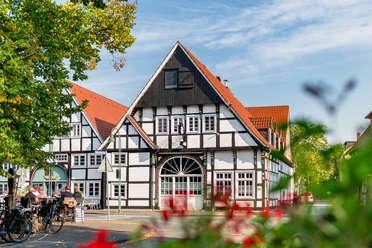 Ankervilla Wiedenbrück Fachwerkhaus mit roten Dächern und blühenden Pflanzen im Vordergrund an einem sonnigen Tag.