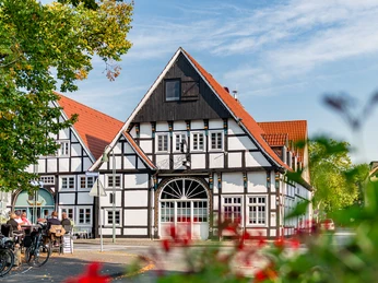 Ankervilla Wiedenbrück Fachwerkhaus mit roten Dächern und blühenden Pflanzen im Vordergrund an einem sonnigen Tag.