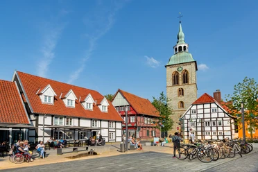 Adenauerplatz Wiedenbrück Historische Fachwerkhäuser und eine Kirche mit grünem Turm bei blauem Himmel in einer Fußgängerzone.