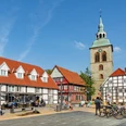 Adenauerplatz Wiedenbrück Historische Fachwerkhäuser und eine Kirche mit grünem Turm bei blauem Himmel in einer Fußgängerzone.