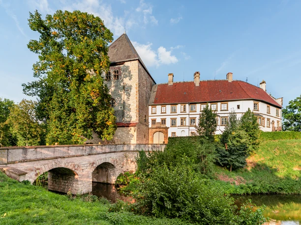 Schloss Rheda Historisches Schlossgemäuer mit Brücke, umgeben von üppigem Grün und klarem Himmel im Sommer.
