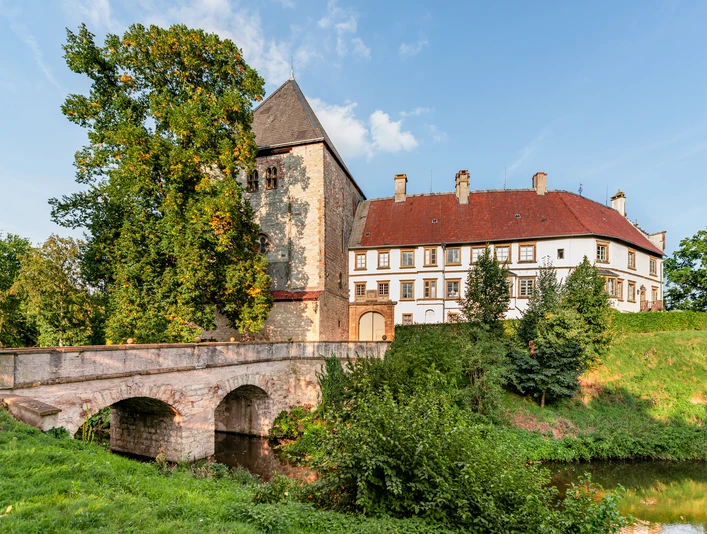 Schloss Rheda Historisches Schlossgemäuer mit Brücke, umgeben von üppigem Grün und klarem Himmel im Sommer.