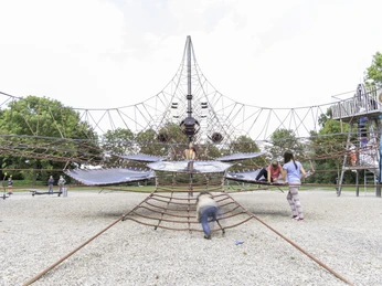 Kinder spielen auf einem großen, netzartigen Klettergerüst in einem sonnigen Park.