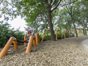 Ein langer, orangefarbener Kletterparcours im Wald auf einem Boden aus Holzhackschnitzeln.