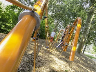 Kinderspielplatz mit leuchtend orangefarbenen Klettergerüsten, umgeben von Bäumen und Holzspänen.