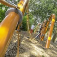 Motorik-Trail an der Mittelhegge Kinderspielplatz mit leuchtend orangefarbenen Klettergerüsten, umgeben von Bäumen und Holzspänen.