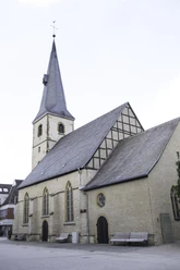 Historische Kirche mit gotischen Fenstern und hohem Turm, umgeben von einer ruhigen Platzfläche.