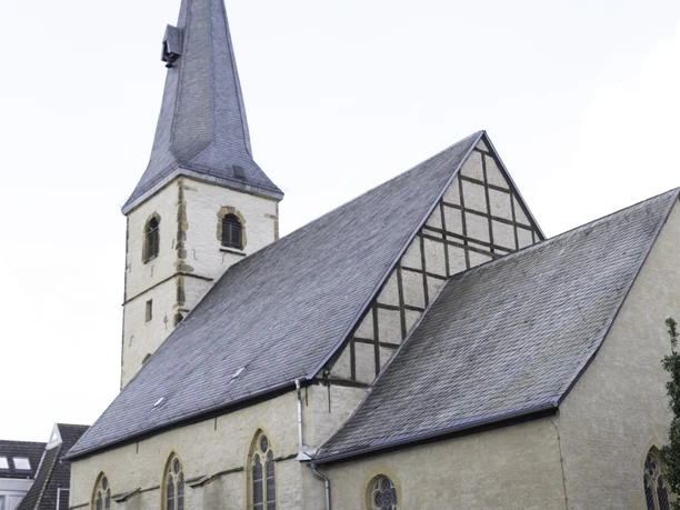 Historische Kirche mit gotischen Fenstern und hohem Turm, umgeben von einer ruhigen Platzfläche.