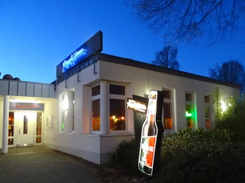 Roadhouse-Aussen.jpg Bar im Abendlicht mit hell erleuchtetem Eingangsbereich und leuchtenden Bierflaschenwerbung.