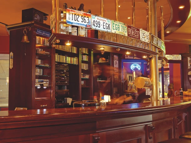 Eine gemütliche Bar mit Holztheke, alten Nummernschildern an der Wand und warm beleuchtetem Ambiente.