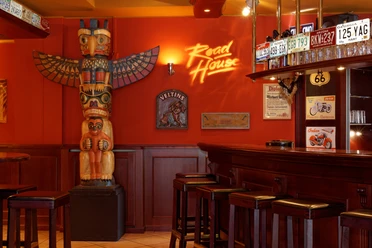 Eine rustikale Bar im amerikanischen Stil mit Totempfahl und Nummernschildern an roten Wänden.