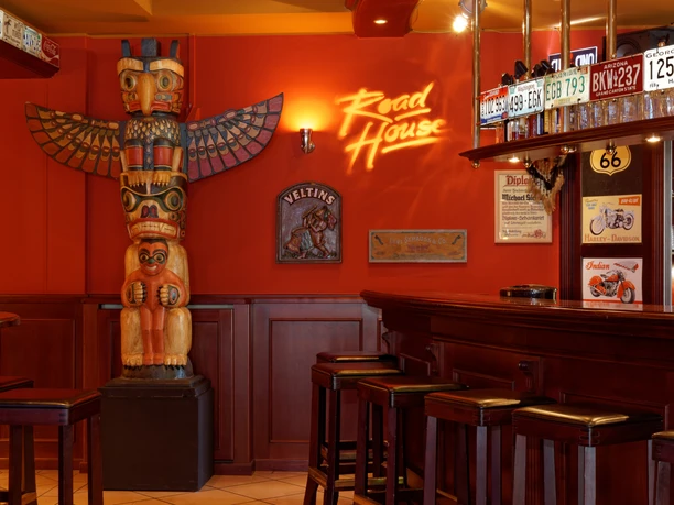 Eine rustikale Bar im amerikanischen Stil mit Totempfahl und Nummernschildern an roten Wänden.