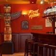 Roadhouse-Innen-03.jpg Eine rustikale Bar im amerikanischen Stil mit Totempfahl und Nummernschildern an roten Wänden.