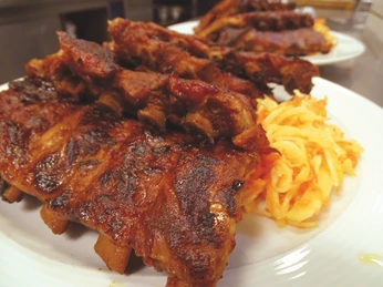 Gegrillte Schweinerippchen auf einem Teller, begleitet von einer Portion cremigem Krautsalat.