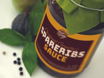 Ein Glas Spareribs-Sauce mit gelbem Etikett, dekorativ mit Basilikumblättern und einer Feige inszeniert.