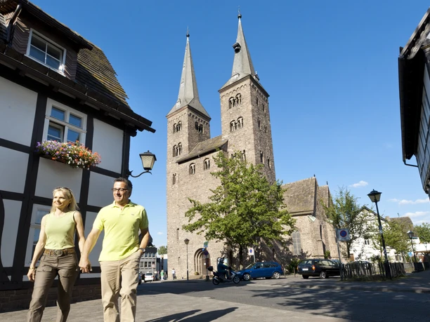 Zwei Personen spazieren an einer historischen Kirche mit markanten Doppeltürmen vorbei.