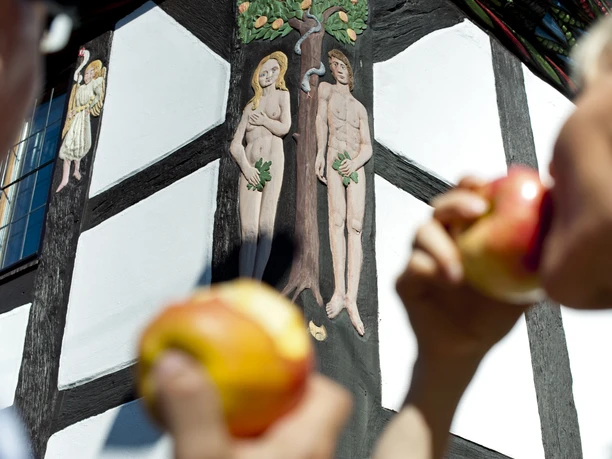 hx-stadtentdecken-andreashub (3).jpg Fachwerkhaus mit Relief von Adam und Eva; im Vordergrund Personen mit Äpfeln in den Händen.