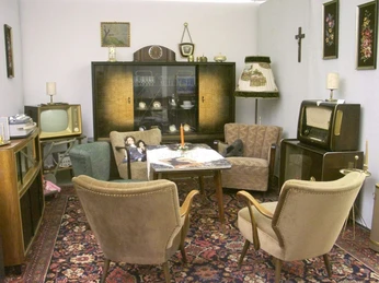 Ein Wohnzimmer im Retro-Stil mit Vintage-Möbeln, Teppich, alter Fernseher und Schrankwand.