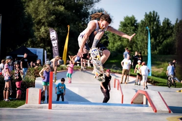 Skatepark "Altes Klärwerk" Ein Skateboarder führt in einem lebhaften Skatepark bei sonnigem Wetter einen Sprungtrick aus.