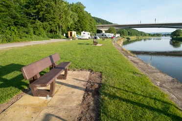Vlothoer Hafen, vorne eine Bank, dann eine Wiese mit Wohnmobilen. Hinten ist die Weserbrücke