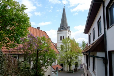 Kirchturm von St. Johannis ragt zwischen rot gedeckten Dächern empor, umgeben von blühenden Bäumen.