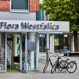 Ein Eingang zur Tourist-Information Flora Westfalica mit zwei Fahrrädern vor modernen Gebäuden.