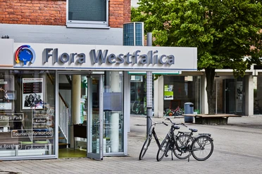 Tourist-Info Rheda-Wiedenbrück Ein Eingang zur Tourist-Information Flora Westfalica mit zwei Fahrrädern vor modernen Gebäuden.