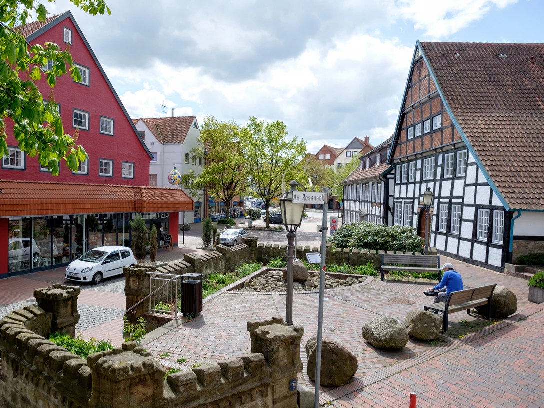 Ein beruhigender Platz mit einer Straßenlaterne, roten und weißen Fachwerkhäusern, und einem Sitzbereich.