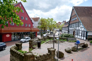 Roseneck Ein beruhigender Platz mit einer Straßenlaterne, roten und weißen Fachwerkhäusern, und einem Sitzbereich.
