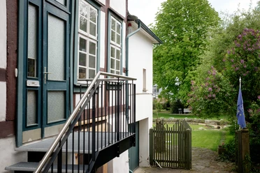 Historische Eingangstreppe führt zu einem zweistöckigen Fachwerkhaus; Garten im Hintergrund mit Flieder.