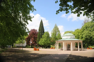 Brunnentempel mit Musikmuschel_02®GesUndTourismus Horn-Bad Meinberg GmbH.JPG Brunnentempel im Park mit grünem Dach, umgeben von Bäumen und einem klaren, blauen Himmel.