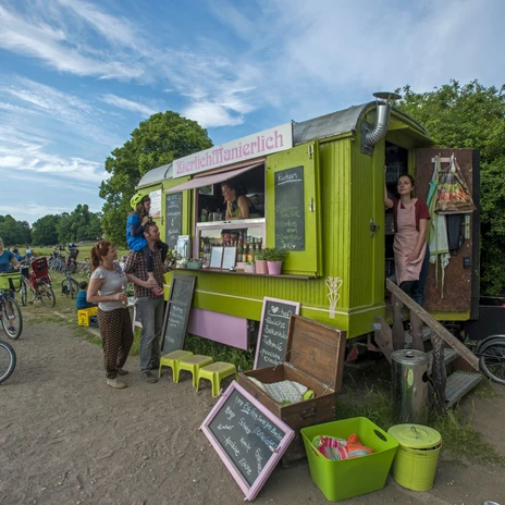 Leipzig, Sachsen, Deutschland. 07.06.2015. Zierlich Manierlich Ð Ein Imbiss im Zirkuswagen. Rollende Bio-Imbissbude am Elsterwehr. Der bei gutem Wetter geoeffnete ehemalige Zirkuswagen bietet Kuchen und Snacks sowie Getraenke an. Verkaufssituation mit Eltern und Kindern. Engl: Leipzig, Saxony, Germany. 07.06.2015. Zierlich Manierlich - Snack bar in a former circus wagon. It is open if the weather is fine. The friendly staff offer homemade cakes, snacks and beverages. Sales situation with parents and children. © copyright: Peter Hirth / Loessniger Strasse 22 / D-04275 Leipzig / Germany phone +49 3412124769 mobil +49 171 2774414 / e-mail: hirthfoto@aol.com / www.peterhirth.de / Bankverbindung: Hamburger Sparkasse / IBAN DE2320050550 / BIC HASPDEHHXXX